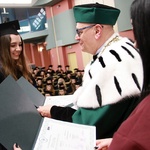 absolwenta w birecie odbiera dyplom z rąk rektora w oficjalnym stroju