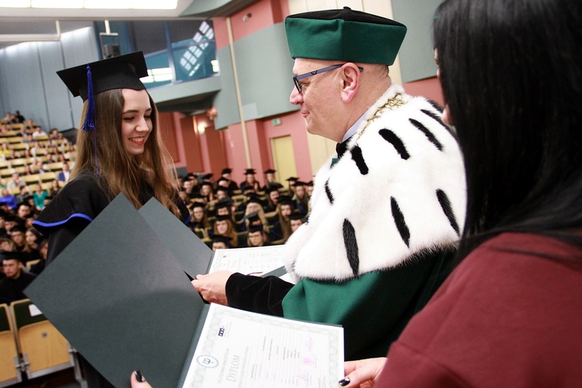 Absolwentka w birecie odbiera dyplom z rąk rektora w oficjalnym stroju
