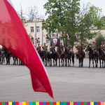 Szereg ułanów na koniach, na pierwszym planie powiewa biało-czerwona flaga