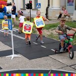 Grupa dzieci jeździ rowerami i biega po matach symulujących ulice ze znakami drogowymi
