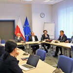 Stół konferencyjy, przy którym siedza sygnatariusze porozumienia. W tle pod ścianą flagi: RP i UE.