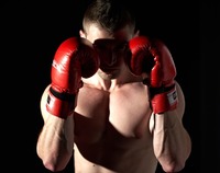 Bokser stojący na czarnym tle, jego twarz spowita w cieniu rzucanym przez czerwone rękawice bokserskie