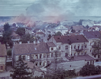 Archiwalne zdjęcie getta białostockiego z 1943 r. - ciąg kamienic z powybijanymi szybami w oknach, nad dachami unosi się dym.