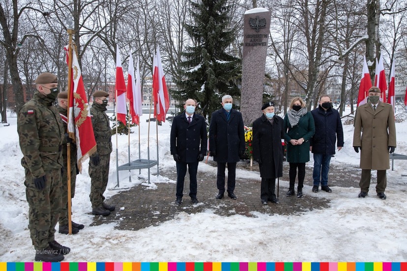 Przed pomnikiem Armii Krajowej oraz biało-czerwonymi flagami stoją m.in. władze Województwa Podlaskiego, wojewoda oraz wojskowy poczet sztandarowy