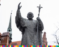 Pomnik, na którym papież podnosi prawą dłoń, w lewej trzyma krzyż.