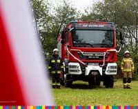 Wóz strażacki obok którego stoi dwóch strażaków