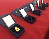 Złote odznaki „Za opiekę nad zabytkami” w pudełkach ozdobnych leżą na czerwonym materiale