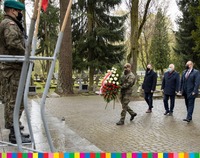Trzech mężczyzn wraz z żołnierzem składają wieniec pod pomnikiem na cmentarzu