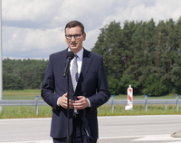 Premier Mateusz Morawiecki stoi przy mikrofonie na tle nowo oddanej do użytku drogi