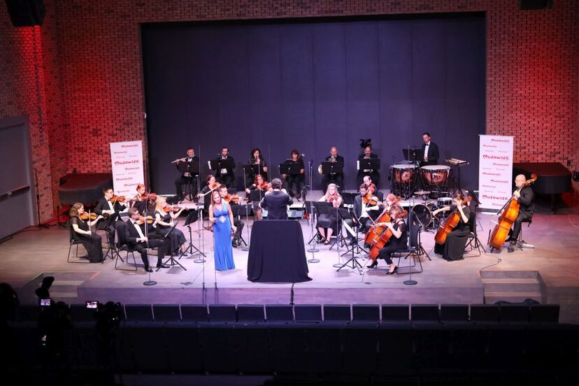 Muzycy filharmonii na scenie. Po srodku solistka w błękitnej sukni.