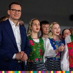 Premier Mateusz Morawiecki. Obok kobiety w strojach ludowych śpiewają
