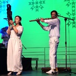 Kobieta i mężczyzna ubrani na biało grają na instrumentach na scenie