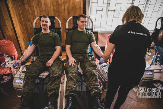 Dwóch żołnierzy w trakcie pobierania krwi. Obok stoi kobieta.