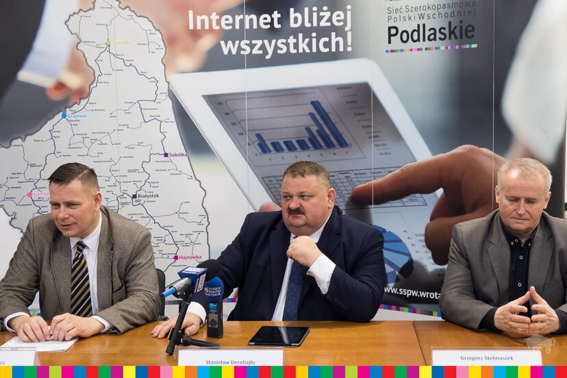 przy stole w sali konferencyjnej siedzą (od lewej): dyrektor z NASK, wicemarszałek i dyrektor z urzędu marszałkowskiego. Na pierwszym planie mikrofony redakcji radia i tv