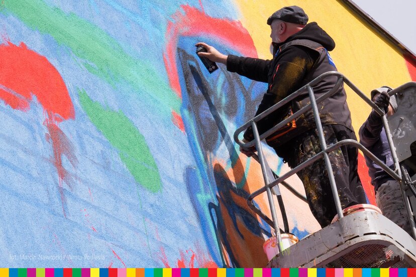 Artysta na podnośniku maluje mural sprayem na ścianie bloku