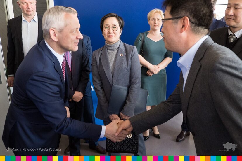 Minister wita się podając dłoń z prezesem firmy Samsung, w tle pani Ambasador Korei