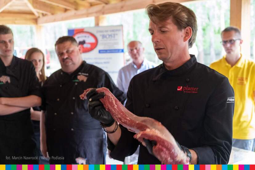Karol Okrasa prezentuje sztukę mięsa, w tle uczestnicy warsztatów kulinarnych