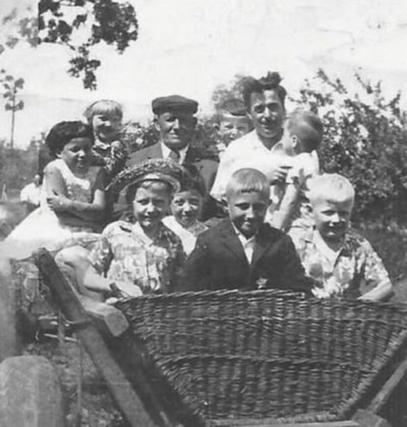 Czarno-biała fotografia przedstawiająca grupę dzieci z na drewnianym wozie