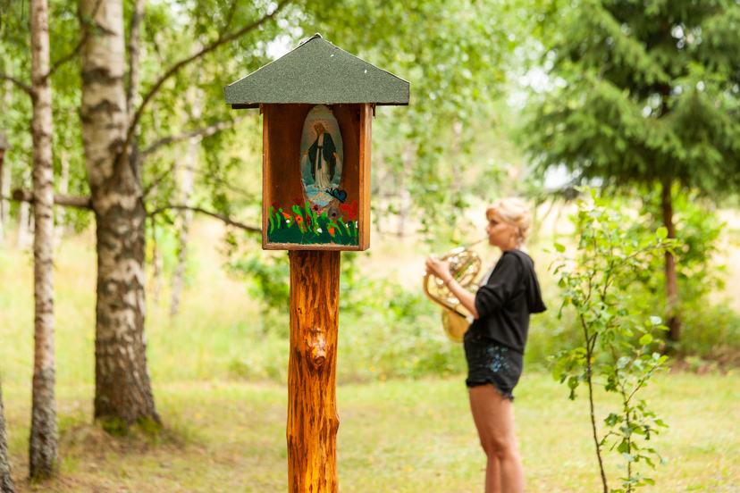 Warsztaty waltornistów w Teremiskach 2019 - dziewczyna z waltornią gra przy leśnej kapliczce