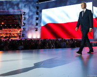 Prezydent idzie po scenie, na dole publiczność, za nią ekran z biało-czerwoną flagą. fot: Igor Smirnow/KPP