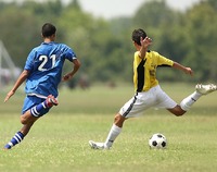 Dwóch piłkarzy ( jeden w niebieskim, drugi w żółtym stroju) w biegu do piłki