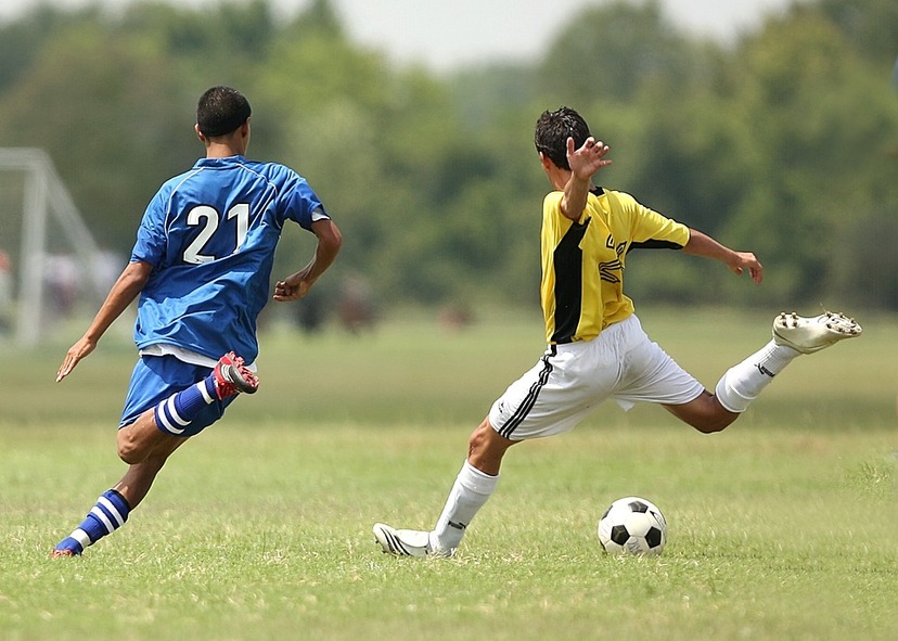 Dwóch piłkarzy ( jeden w niebieskim, drugi w żółtym stroju) w biegu do piłki