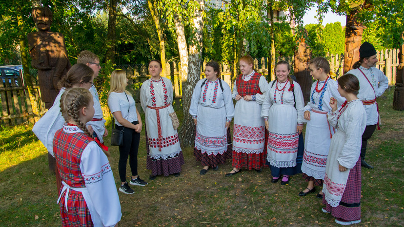 Zespół Żemerwa - ubrane w stroje białoruskie (biało-czerwone) kobiety stoją w półokręgu z uczestnikami warsztatów śpiewaczych. W tle las.