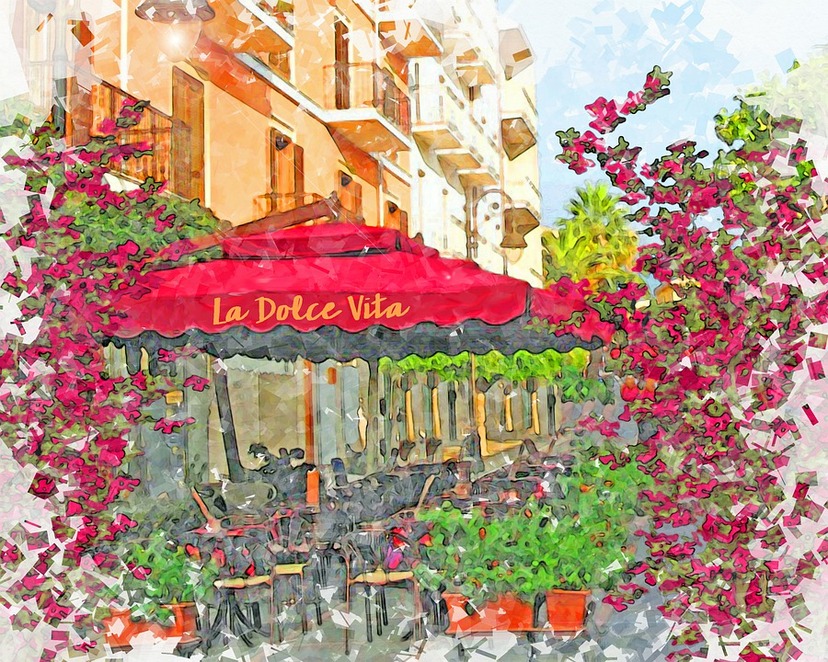 Włoska kawiarenka na ulicy , na pierwszym planie czerwony parasol z żółtym napisem La dolce vita, obok kwitnące, różowe kwiaty.