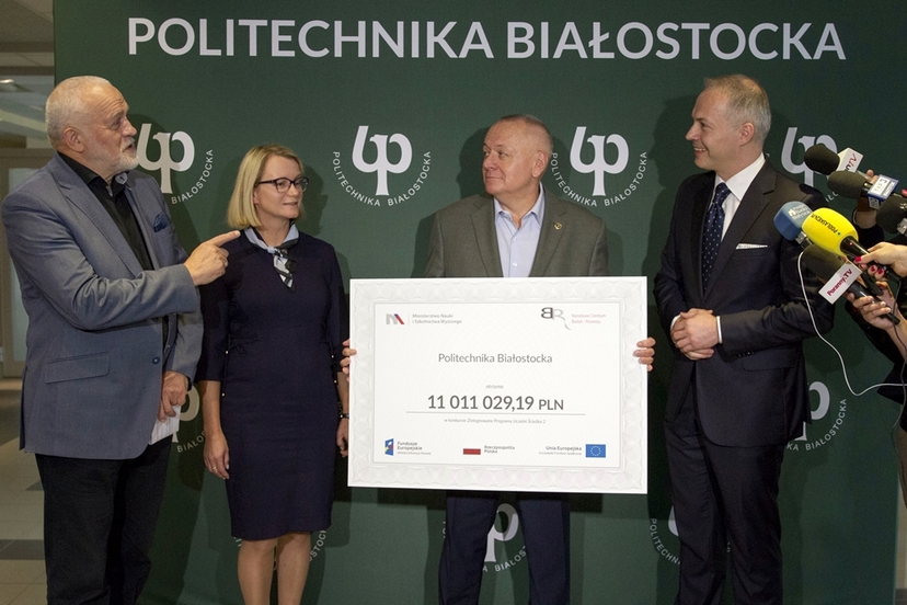 Cztery osoby prezentujące czek na ściance z logo Politechniki.