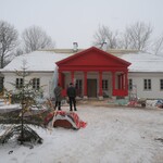 Budynek zimową porą z czerwonymi kolumnami. Przed budynkiem znajduje się choinka oraz stoi dwóch mężczyzn.