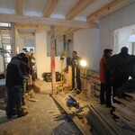 Na budowie. W środku remontowanego budynku znajduje się kilku robotników, obok nich leżą elementy drewniane.
