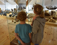 Dwójka dzieci ogląda stojące na półce  wyroby ludowe z gliny i ze słomy.