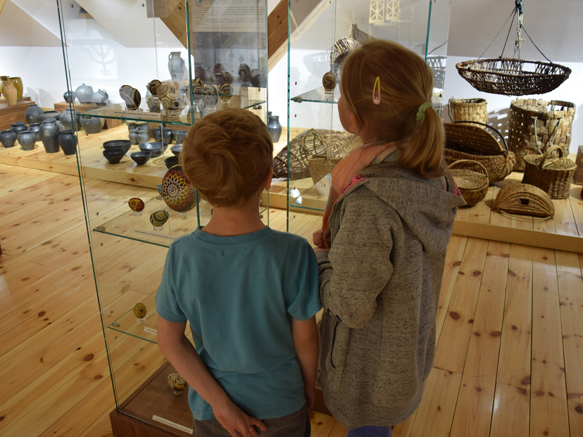 Dwójka dzieci ogląda stojące na półce  wyroby ludowe z gliny i ze słomy.