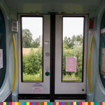 Zamknięte drzwi w pociągu, za nimi krajobraz pełen zieleni