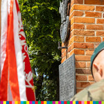 Przybliżenie na tablicę pamiątkową przy której stoi żołnierz. Widać fragment flagi.