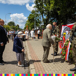 Starszy mężczyzna składający kwiaty pod tablicą pamiątkową. Za nim stoi starsza kobieta oraz Sekretarz Województwa Tomasz Szeweluk.