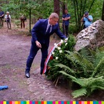 Marek Malinowski składający wieniec pod kamiennym pomnikiem. W tle las.