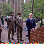 Leśnicy oraz Marek Malinowski przypatrujący się tablicy pamiątkowej. W tle las