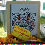 Na pierwszym planie ramka w niej grafika z serduszkiem w kwiaty i napisem KGW Szeroka Struga.
