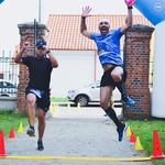 Dwóch mężczyzn skacze w trakcie biegu z wyciągniętymi do góry rękoma przebiegając linię mety