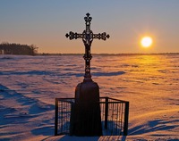 przydrożny krzyż na tle zimowego krajobrazu; w tle zachodzące słońce
