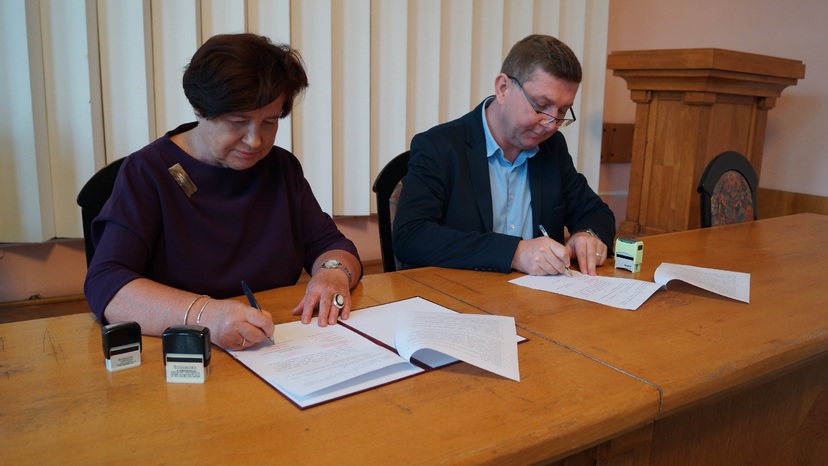 Kobieta i mężczyzna za stołem podpisują umowy.