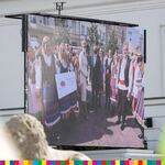 Ekran telebimu z parą prezydencką stojącą w otoczeniu osób w strojach ludowych.