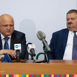 Stanisław Derehajło, wicemarszałek województwa siedzi obok mężczyzny mówiącego do mikrofonów.