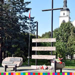 Widok ogólny na pomnik upamiętniający zesłańców syberyjskich i kościół w otoczeniu drzew.