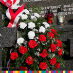 Wieniec z biało - czerwonych kwiatów złożony na mogile żołnierskiej.