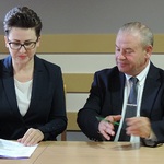 2 osoby za stołem. Po prawej wicemarszałek Olbryś, po lewej wicestarosta Maria Dziekońska podpisuje umowę. 