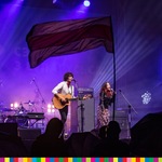 Kobieta i mężczyzna śpiewający na scenie oraz powiewająca flaga Białorusi