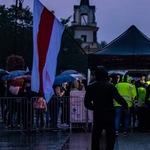 Flaga Białorusi oraz grupa ludzi stojąca pod parasolami
