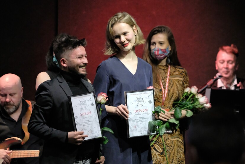 Dwoje nagrodzonych uczestników trzyma róże i dyplomy na scenie.